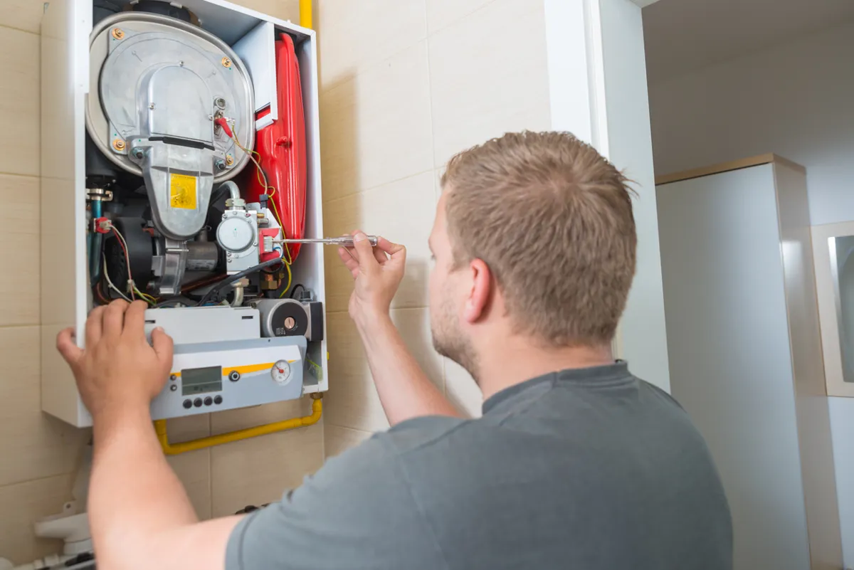 A technician adjusting a heating system mounted on a wall.