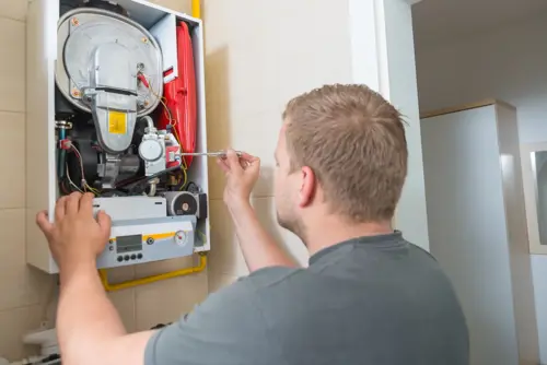 A technician adjusting a heating system mounted on a wall.