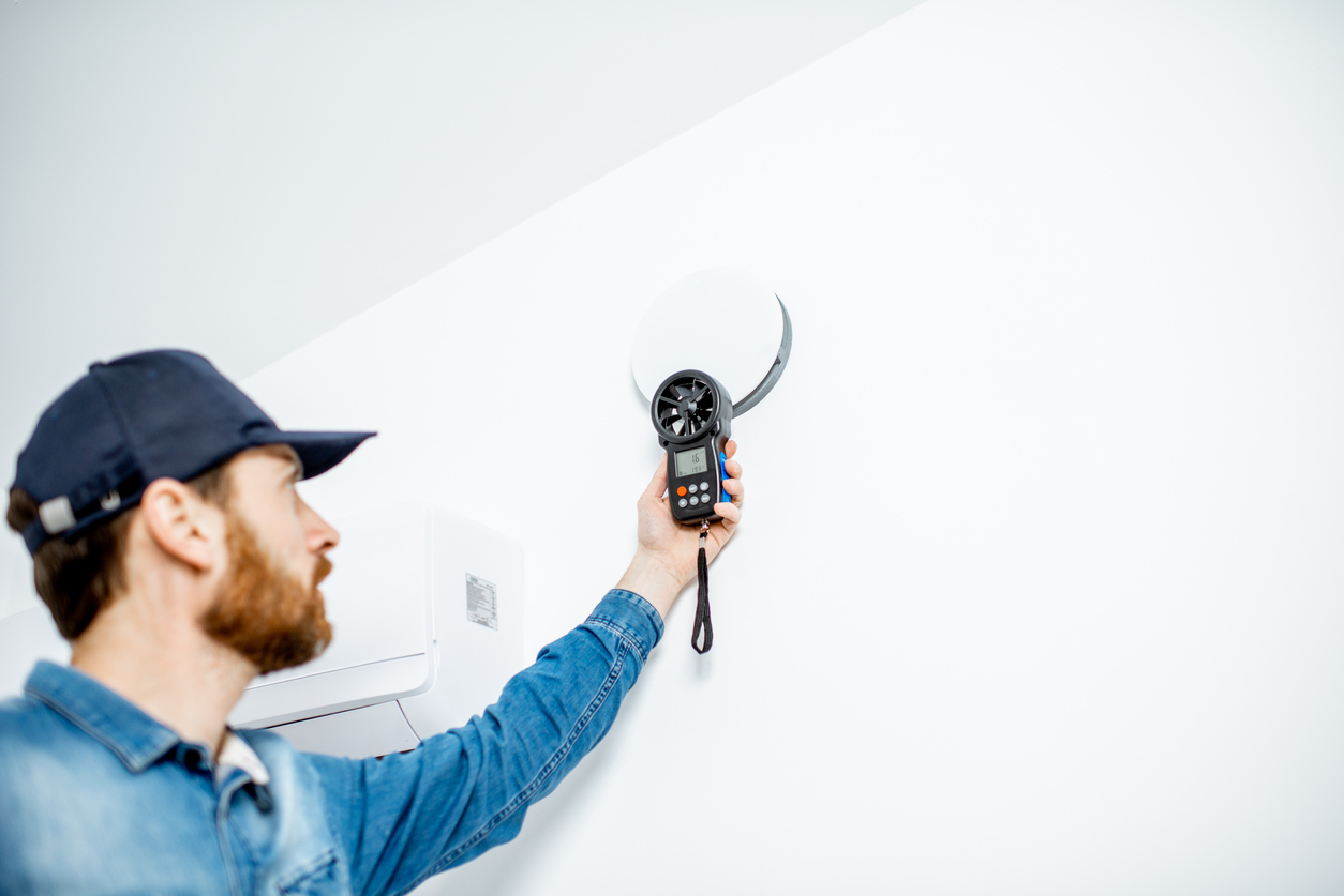 Seattle indoor air quality technician measuring airflow from a home ventilation system with an air meter.
