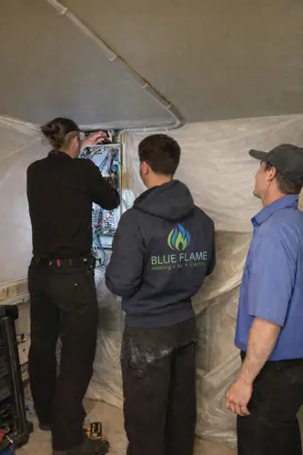 Three tradesmen working on an electrical panel in an unfinished utility room.